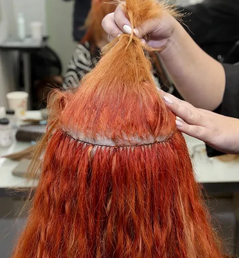 אישה עם שיער ג'ינג'י ארוך, שחלקו העליון מורם, וחושף שורת תוספות שיער המחוברות לקרקפת