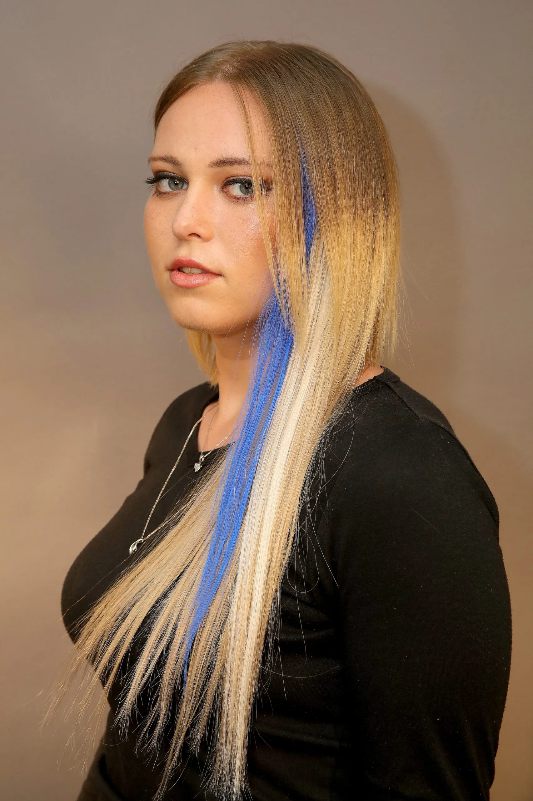 אישה עם שיער בלונדיני ארוך ופס כחול בולט, מדגימה תוספת שיער או צבע